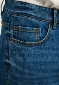 Blå denimjeans med en klassisk design, som har en bakficka, gyllene stygn och en jämn textur.