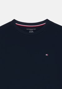Navy blue t-shirt with a crew neck, featuring a small embroidered logo in red, white, and blue. Smooth fabric with a regular fit.