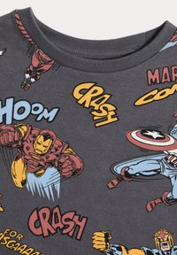Camiseta de algodón gris con estampados de superhéroes y efectos de sonido en colores brillantes, al estilo de cómic. Cuello redondo y mangas cortas.