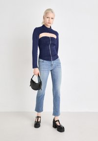 Navy zip-up top with a cutout design, paired with light blue straight-leg jeans. Accessories include a small black handbag and platform shoes.