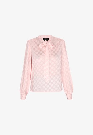 Blouse rose clair à manches longues avec un détail de nœud au col, présentant un motif à pois et une texture de tissu transparent. Cette blouse a des poignets ajustés.