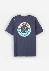 T-shirt en coton bleu marine avec un graphisme circulaire portant le texte "OXBOW STAY ALIVE" et des motifs floraux dans des couleurs pastel. Manches courtes.