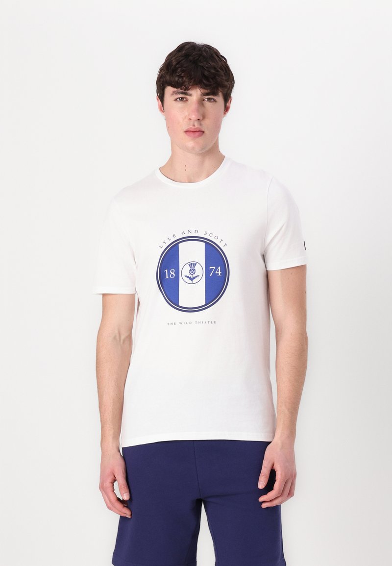 Balta trumpa rankovėmis marškiniai su mėlynu apvaliu logotipu, kuriame užrašyta "LYLE AND SCOTT," "1874" ir šeivamedžio dizainas centre. Lygus paviršius.