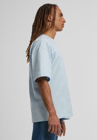 Camiseta de algodón azul claro de manga corta, corte relajado, cuello redondo y textura suave, combinada con jeans de denim.