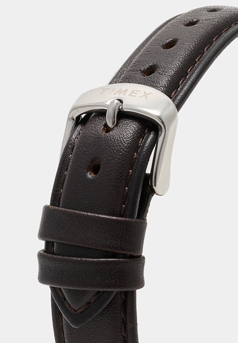 Correa de reloj de cuero marrón con hebilla metálica grabada con "TIMEX" y múltiples agujeros de ajuste.