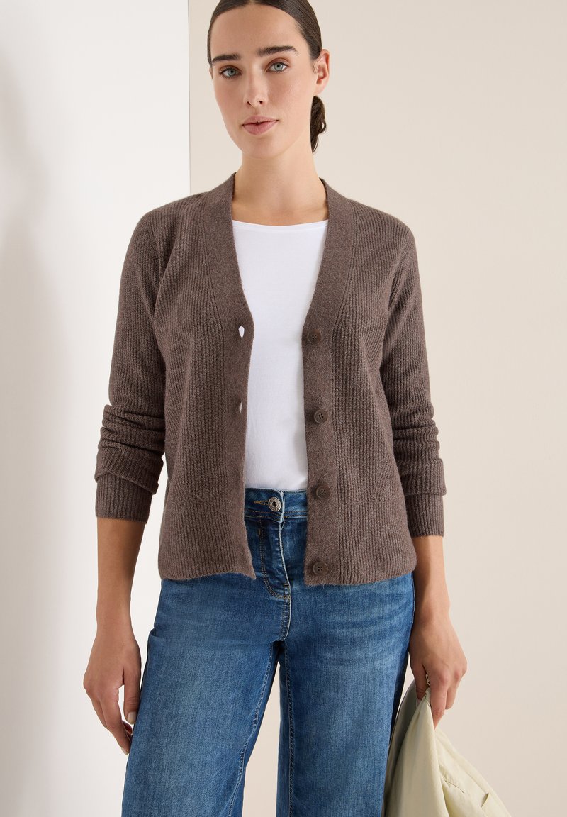 Brun ribbad cardigan i mjukt material, med v-ringning, knappstängning och långa ärmar, kombinerad med blå jeans.