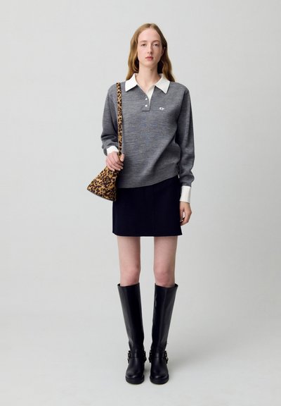 Maglione grigio a maglia con colletto bianco, gonna nera corta e stivali neri fino al ginocchio. Tiene una borsa a tracolla con stampa leopardata.
