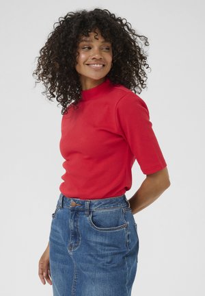 Haut rouge à manches courtes en tissu côtelé, avec un col montant. Associé à une jupe en denim bleue à coupe classique et poches avant.