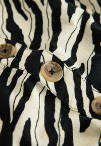 Nahaufnahme eines Stoffes mit schwarz-weißen Zebrasteifen und drei braunen Schildpattknöpfen, die an einer Naht angenäht sind.