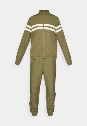Chándal verde oliva con chaqueta con cremallera y puños elásticos. Presenta rayas horizontales blancas en el pecho y pantalones a juego con detalles de logotipo.