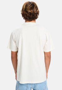 Kortærmet cremet bomulds T-shirt med en afslappet pasform, der har rund hals og et subtilt mærke på den nederste side. Flad bagside.