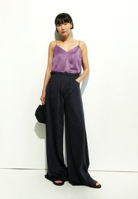 Lila Satin-Camisole mit dünnen Trägern, kombiniert mit luftigen, schwarzen, weit geschnittenen Hosen mit elastischem Bund und seitlichen Taschen.