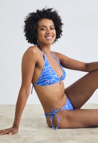 Modrý bikini s trojuholníkovým vrchom a viazanými spodnými časťami, zdobený vzorom vĺn a detailmi. Hladký povrch, nastaviteľné ramienka.