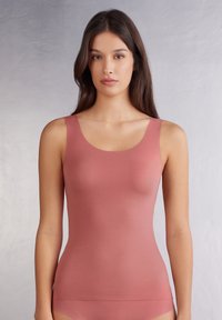 Přiléhavý top bez rukávů z měkké a elastické tkaniny. Má kulatý výstřih, široké ramínka a hladkou, růžovou strukturu.