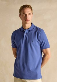 Vīriešu īssleeve polo krekls gaiši zilā kokvilnā, ar klasisku apkakli, trīs pogu slēgšanu un izšūtu logo uz krūtīm.
