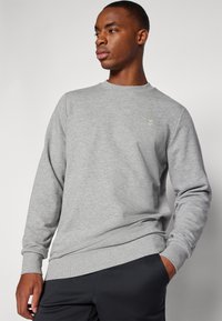 Grauer Sweatshirt mit Rundhalsausschnitt, langen Ärmeln und gerippten Bündchen. Verfügt über ein kleines goldenes Logo auf der Brust und einen lässigen Schnitt.