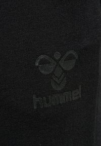 Czarna tkanina z subtelnym, tłoczonym logo Hummel, z stylizowaną trzmielem i nazwą marki poniżej.