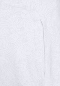 Tejido blanco con un sutil patrón floral en espiral. Incluye un pequeño botón con logo y un bolsillo lateral con costuras decorativas.