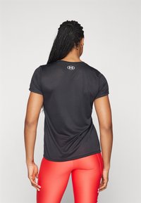 Svart träningströja med kort ärm och rund halsringning, med en logotyp på baksidan. Kombinationen av tröjan med röda leggings. Slät tygstruktur.