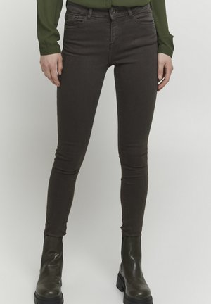 Braune Skinny-Jeans aus Denim mit einem klassischen Fünf-Taschen-Design, subtiler Stickerei und kombiniert mit grünen kniehohen Stiefeln.