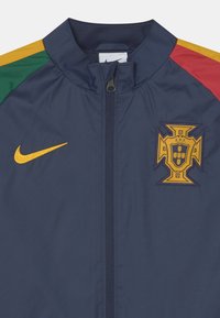 Navy windbreaker jacket with green, yellow, and red accent stripes, featuring a yellow Nike logo and a prominent embroidered Portugal crest.