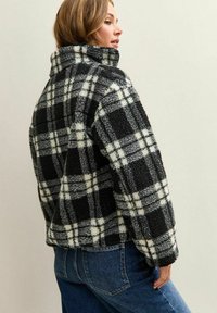 Fleece jack met een zwart-wit geruit patroon. Voorzien van een hoge kraag en een cropped ontwerp. Zachte textuur en een ontspannen pasvorm.