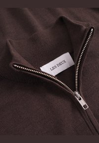 Smeđa zip majica s mekim pletenim teksturom i rebrastim vratom. Oznaka "LES DEUX" nalazi se blizu zatvarača. Detalj srebrnog zatvarača.