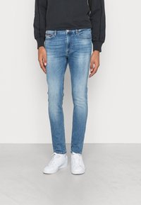 Jeans ajustados de color azul claro, hechos de denim, con un lavado desgastado y diseño estándar de cinco bolsillos, combinados con zapatillas blancas.