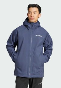 Chaqueta impermeable azul marino con un alto cuello, capucha ajustable, cremallera completa y bolsillos laterales; presenta el logo TERREX en blanco.