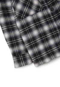 Tessuto a quadri in bianco e nero con una texture morbida. Presenta linee bianche che formano quadrati e rettangoli, con sfumature irregolari per un effetto ombra.