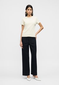 Κρεμ κοντομάνικη μπλούζα συνδυασμένη με μαύρο, ψηλόμεσο παντελόνι φαρδιάς γραμμής. Το μοντέλο φοράει λευκές γόβες με μυτερή μύτη. Απλός, καθαρός σχεδιασμός.