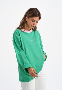 Groen en wit gestreepte oversized sweatshirt met een roze kraag, lange mouwen en een klein geborduurd detail aan de voorkant.