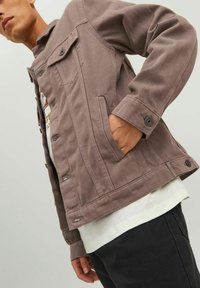 Giacca in denim marrone chiaro con chiusura frontale a bottoni, due tasche sul petto e tasche laterali. Presenta una vestibilità rilassata e un tessuto leggermente testurizzato.