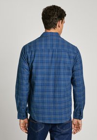Camicia a scacchi blu con maniche lunghe, polsini con bottoni e colletto. Il tessuto sembra morbido; il design presenta motivi a scacchi in blu scuro e chiaro.