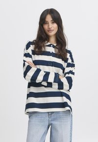 Marineblau-weiß gestreiftes Langarmhemd mit Kragen und drei Knöpfen, kombiniert mit hellblauen Jeans. Standardpassform mit seitlichen Schlitzen.