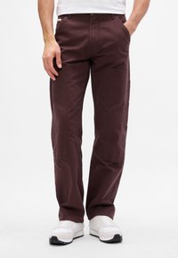 Pantaloni cargo bordeaux con due tasche frontali, design a gamba dritta e tessuto strutturato. Indossati con sneaker bianche.