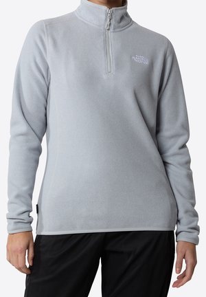 Lysegrå fleece-trøje med lange ærmer og kvart lynlås med The North Face-logo på brystet, båret med sorte bukser.