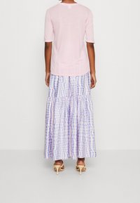 Top rosa chiaro aderente, abbinato a una gonna lunga a balze con un motivo a quadretti nei toni pastello del viola e azzurro. Tessuto morbido con una vestibilità comoda.