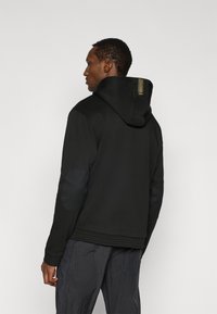 Μαύρο φούτερ με κουκούλα, με ανάγλυφη πίσω επιφάνεια και επιθέματα στους αγκώνες. Διαθέτει λογότυπο με χρυσές λεπτομέρειες στον λαιμό. Σχεδιασμός με άνετη εφαρμογή.