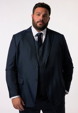 Traje de tres piezas en color navy con un acabado texturizado. Chaqueta de un solo botón, con solapas de muesca y chaleco a juego con cinco botones. Camisa blanca y corbata oscura.