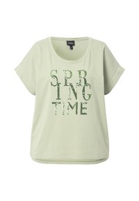 Camiseta de manga corta verde claro con el texto "PRIMAVERA" en lentejuelas verdes. Tejido suave con un corte relajado y cuello redondo.