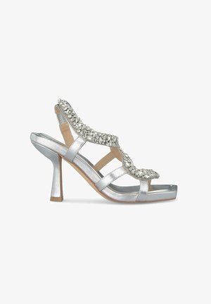 Silberne High-Heel-Sandale mit einer glatten metallischen Oberfläche, dekorativen Strassakzenten entlang des Riemens und einem Blockabsatzdesign.