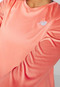 Lichtroze sportieve lange mouwen shirt met een gestructureerd patroon, ronde halslijn en een reflecterend logo op de borst. Zachte stof.