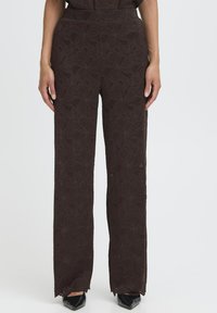 Rudos gėlėmis raštuoti plačiakojai džinsai su tekstūriniu paviršiumi ir plokščiu juosmeniu, su nerištais kraštais ir modelio rankomis šonuose.