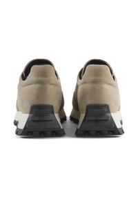 Smeđe antilop sportske cipele s crnom gumenom potplatom i debelim, robusnim uzorkom. Imaju podignuti potplat i kontrastnu bijelu srednju potplatu.