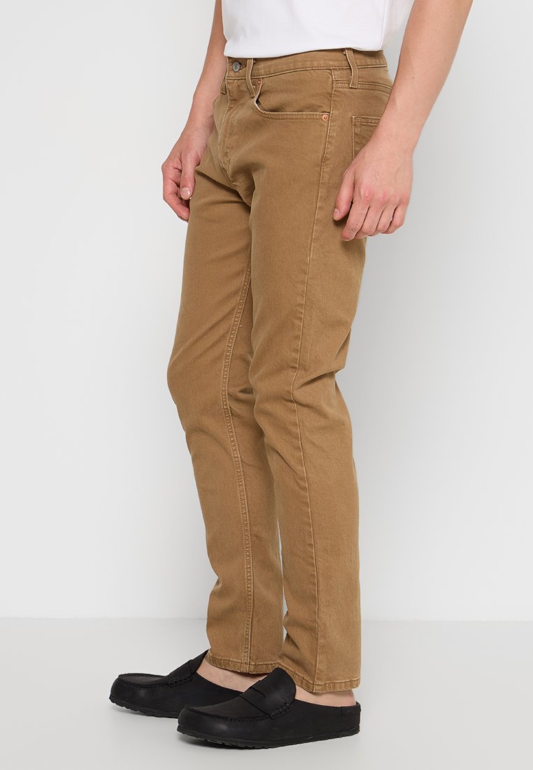 Pantaloni in cotone beige con vestibilità slim, cuciture visibili e tasche frontali. Indossati con scarpe nere slip-on.