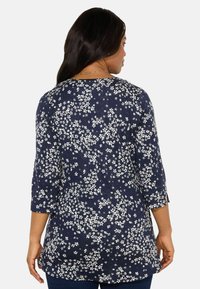 Merenneitinen paita, jossa on valkoinen kukkakuosi, kolme neljäsosaa hihat ja pyöreä kaula-aukko. Rentouttava istuvuus ja pehmeä rakenne.