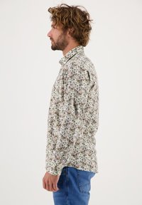 Bloemenoverhemd met een lichtgroene achtergrond, versierd met kleine meerkleurige bloemen en een klassieke kraag. Gekoord met blauwe spijkerbroek.