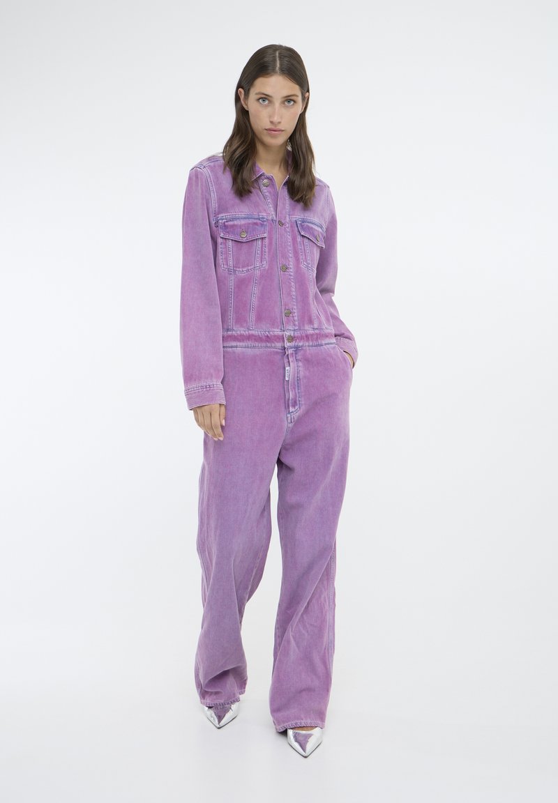Vijolični denimski kombinezon z dolgimi rokavi, dvema sprednjima žepoma in gumbnim zapiranjem. Ohlapen kroj z rahlo zbledelim vzorcem. Srebrni špičasti pete.