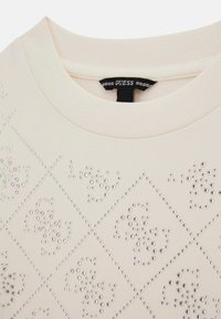 Felpa beige chiaro con collo rotondo, caratterizzata da un motivo a rombi di strass metallici. La tessitura del tessuto appare liscia e morbida.
